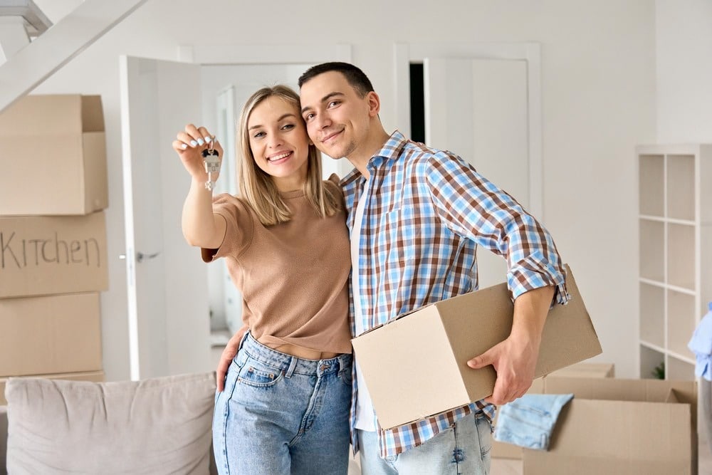 Couple holding keys in new home from Spartan Property Estate Agents, smiling with moving boxes.